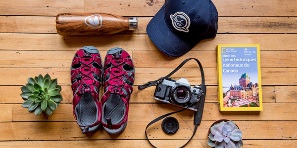 Un arrangement d'équipement comprenant une bouteille d'eau, une casquette, des sandales, une caméra et un guide de voyage.