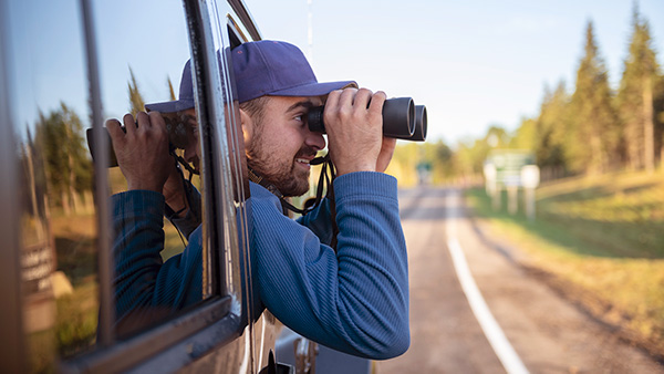 A visitor uses binoculars to watch for wildlife from a vehicle off the Parkway in Elk Island National Park.