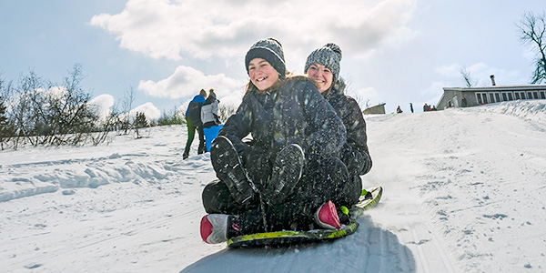 A mother and daughter enjoy sledding on a hill in Kouchibouguac National Park.
