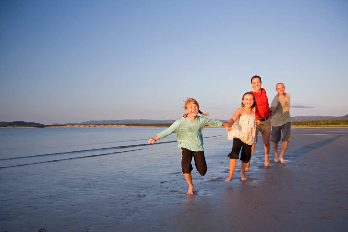Des visiteurs courent sur la plage de Shallow Bay Beach en se tenant par la main. Parc national du Gros-Morne.