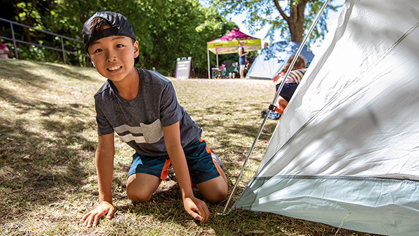 Un enfant souriant monte une tente dans le cadre d’une activité d’initiation au camping le long du canal Rideau.