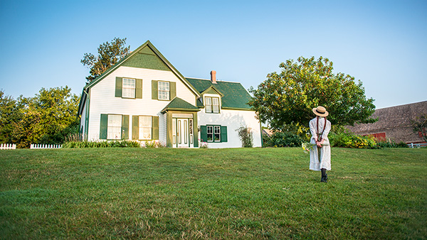 A Parks Canada interpreter dressed as Anne of Green Gables walks on the front lawn of Green Gables Heritage Place.