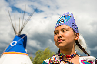 Hailey Saulteaux, membre de la Première Nation O'Chiese portant une tenue traditionnelle devant un tipi au lieu historique national Rocky Mountain House.